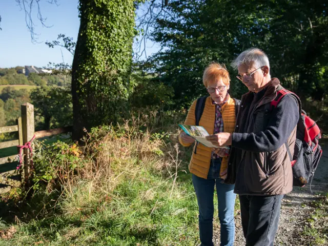 Deux personnes en randonnée consultent une carte près d'un chemin de campagne