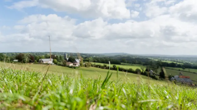 Champ vert avec des maisons et des collines à l'horizon sous un ciel bleu avec des nuages blancs
