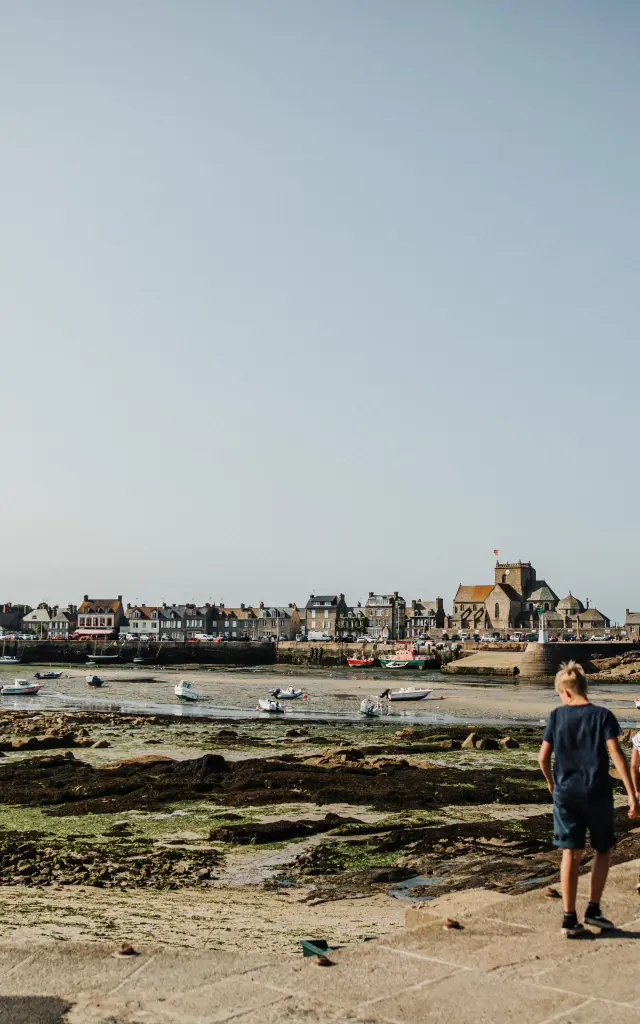 Zwei Personen gehen auf einem Weg am Meer mit Booten im Hintergrund