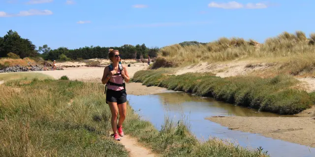 A woman walks on a path near a beach with sand dunes