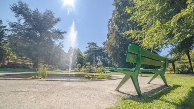 Banc public vert en métal avec dossier triangulaire, installé sur une pelouse en bordure de route