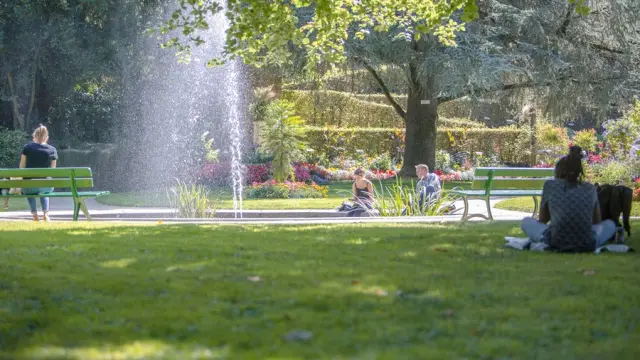 Menschen sitzen auf Bänken in einem öffentlichen Garten mit einem Brunnen im Hintergrund