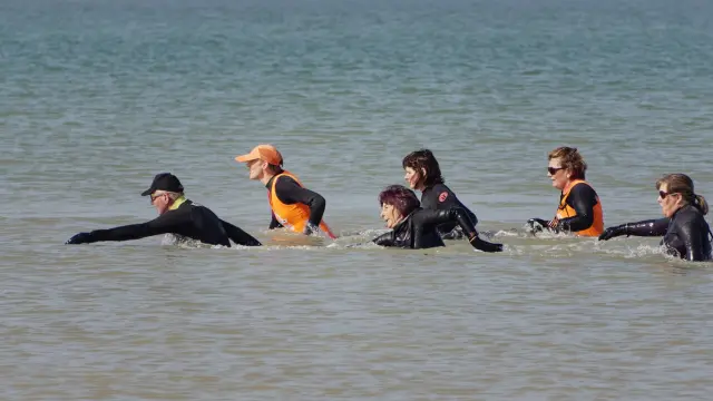 Groupe de personnes en combinaison de surf dans l'eau peu profonde faisant du longe cote