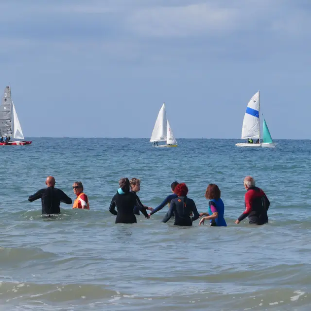 Un groupe de personnes faisant du longe côte en mer avec des voiliers en arrière-plan