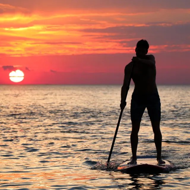 Personne faisant du paddleboard sur l'eau au coucher du soleil
