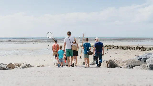 Une famille marchant sur une plage de sable avec des filets pour la pêche à pied à Agon COutainville