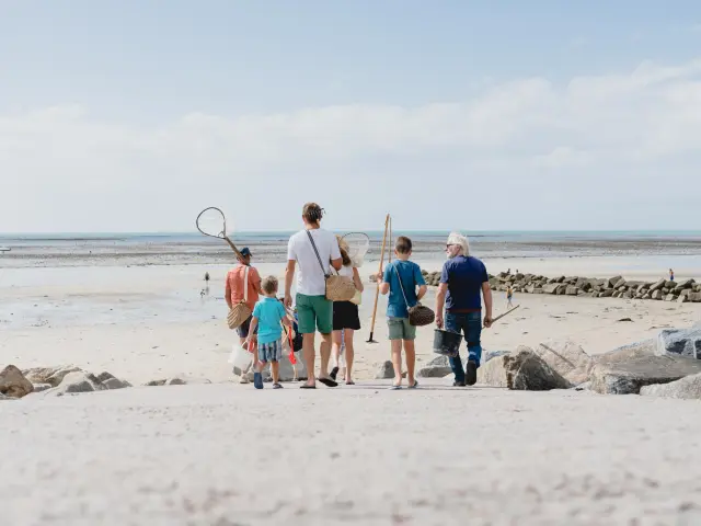 Une famille marchant sur une plage de sable avec des filets pour la pêche à pied à Agon COutainville