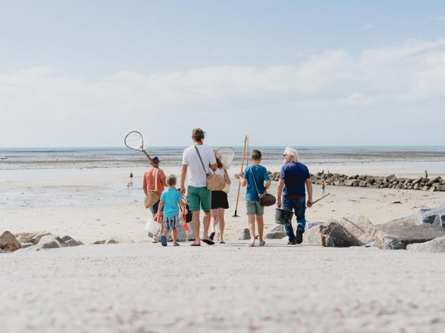 Une famille marchant sur une plage de sable avec des filets pour la pêche à pied à Agon COutainville