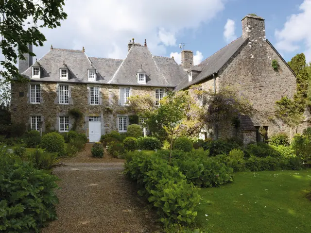 Manoir en pierre avec tourelles et toits en ardoise, entouré d'un jardin verdoyant