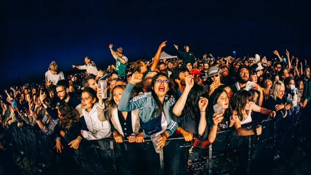 Une foule nombreuse levant les mains en l'air lors d'un concert de nuit au Festival Chauffer dans la noirceur