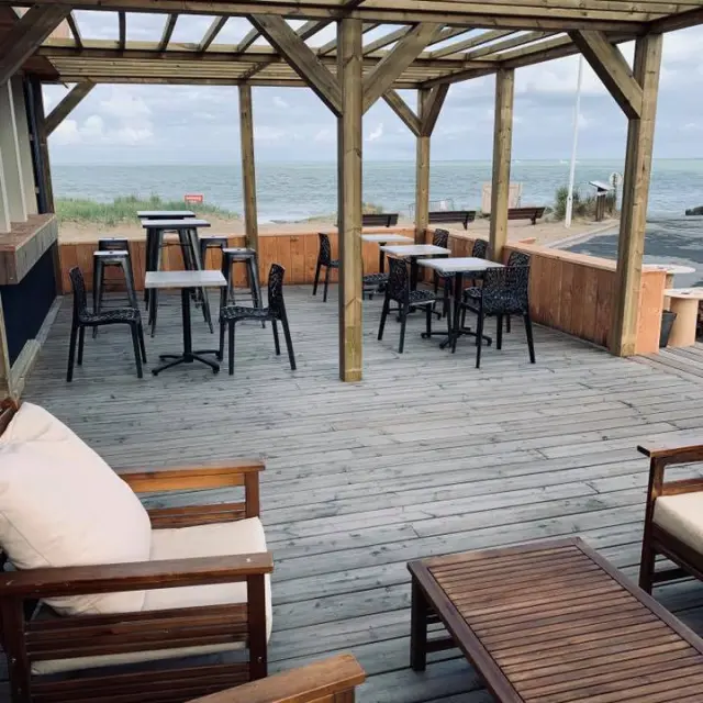 Terrasse en bois avec des tables et des chaises près de la mer : restaurant les dunes