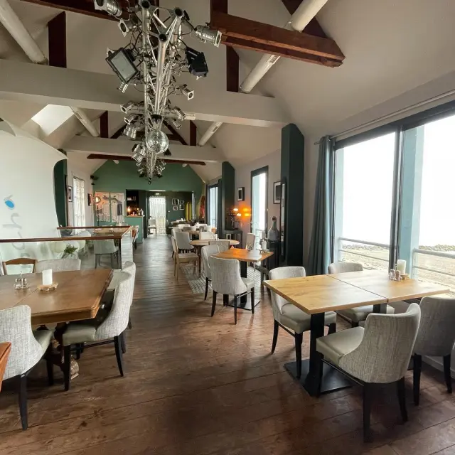 Intérieur du restaurant la plancha avec des tables en bois, des chaises rembourrées et une grande fenêtre offrant une vue sur l'extérieur