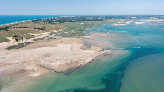 Paysage de dunes de sable blanc bordant un lagon aux eaux turquoise, avec des traces de pas visibles