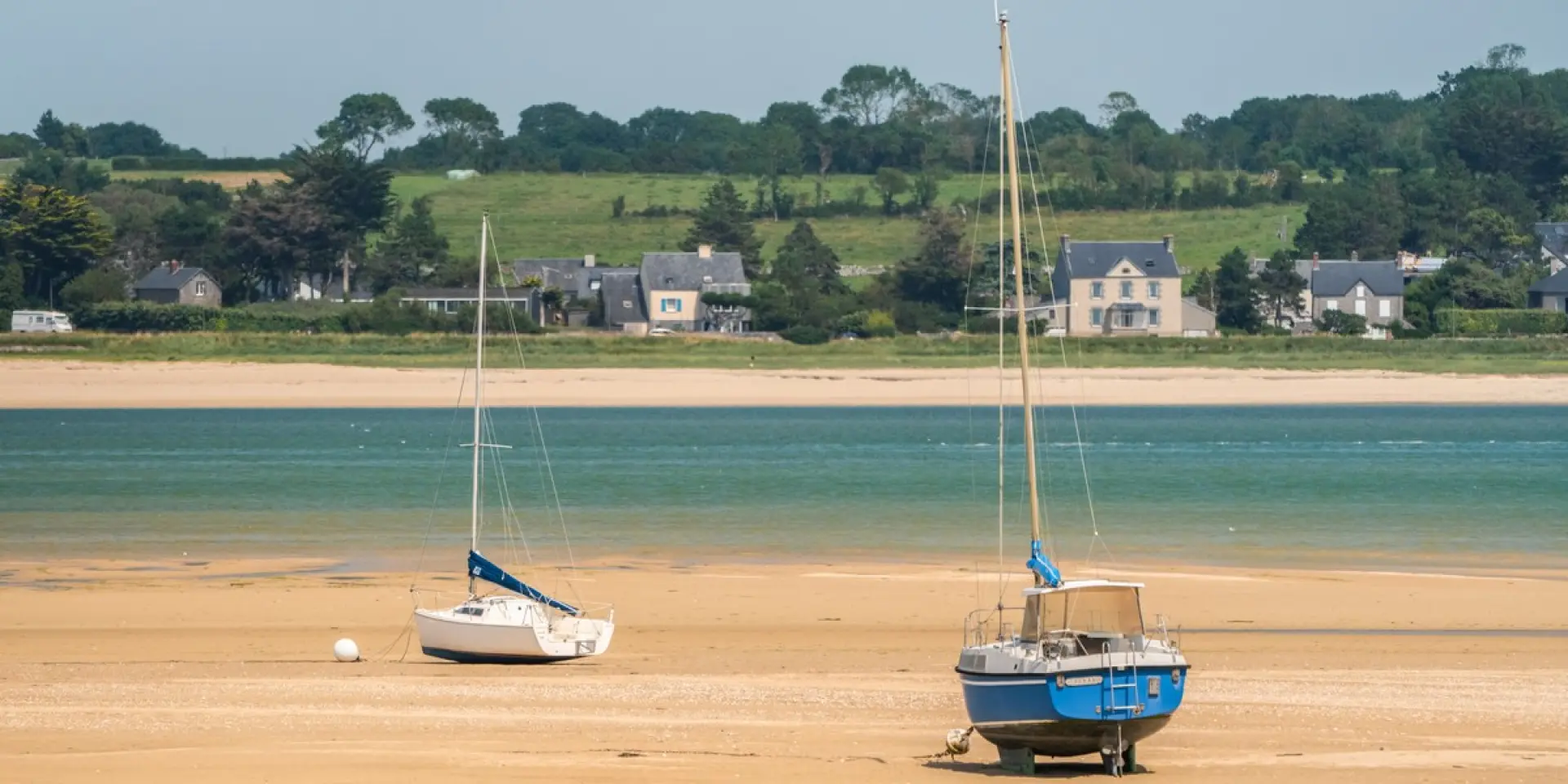 Deux voiliers amarrés sur une plage de sable avec des bâtiments en arrière-plan au crépuscule