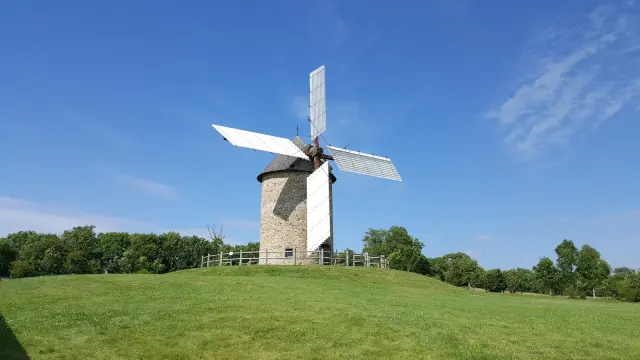 Eine weiße und graue Windmühle auf einem grünen Hügel