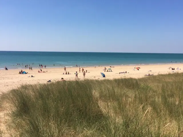Plage de sable avec des gens se baignant et se relaxant sous un ciel bleu clair à Annoville
