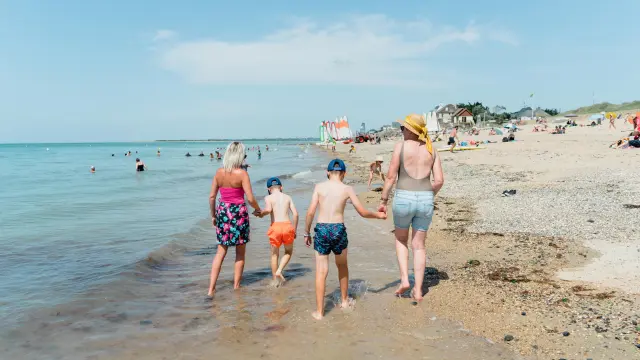 Une famille marche le long de la plage avec deux enfants entre les parents
