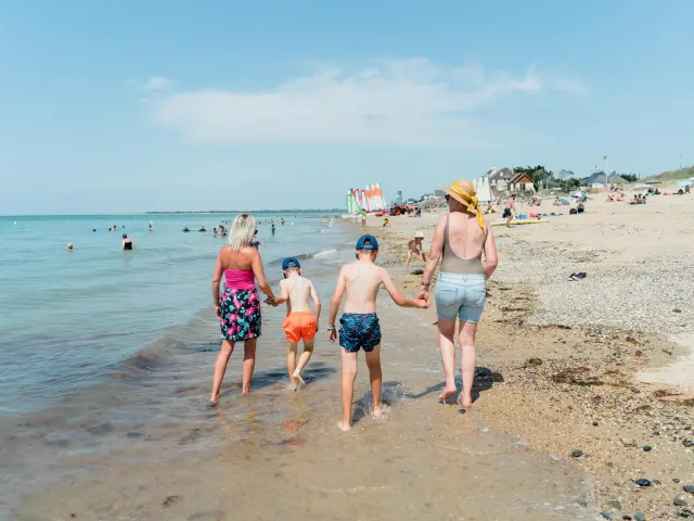 Une famille marche le long de la plage avec deux enfants entre les parents