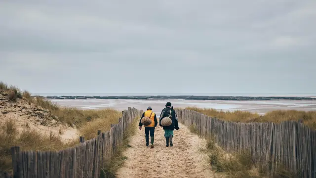 Deux personnes marchant sur un chemin de sable vers la mer à Annoville