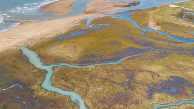 Paysage de dunes et de lagons aux eaux turquoise, avec des reflets du ciel