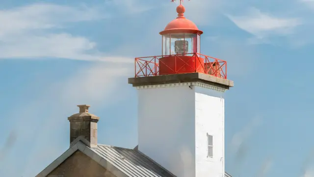 Red and white lighthouse with a red lantern on top, surrounded by greenery by a body of water