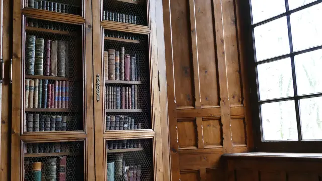 Bibliothèque en bois ancienne avec des étagères remplies de livres et une fenêtre au château de Cerisy La Salle