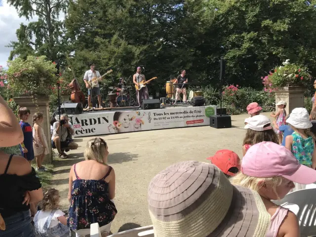 Un groupe de musique joue sur scène devant un public assis au jardin des plantes de Coutances