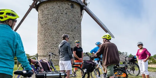 Un groupe de cyclistes en pause devant le moulin en pierre de Gouville sur mer