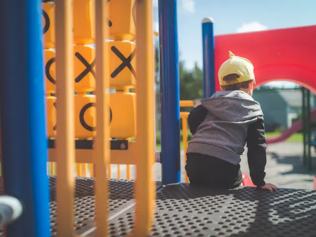 Un enfant portant un chapeau jaune est assis au sommet d'un toboggan dans une aire de jeux