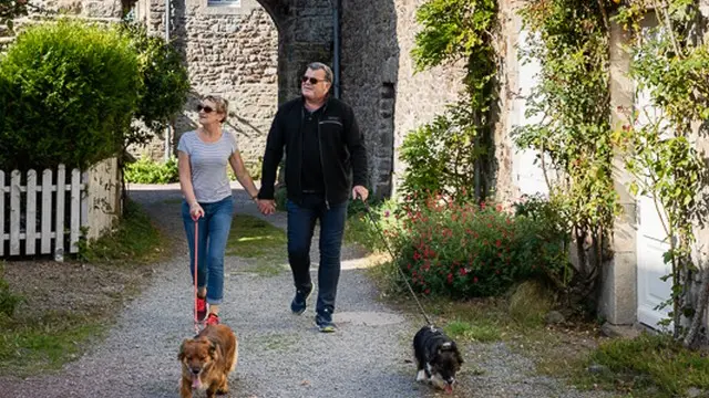 Zwei personen mit zwei hunden in einer gasse zwischen steinhäusern spazieren