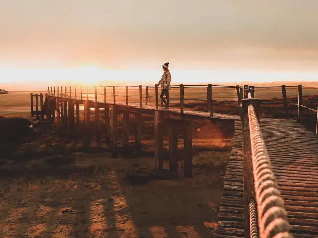 Personne debout sur un ponton en bois au coucher du soleil à la pointe d'Agon