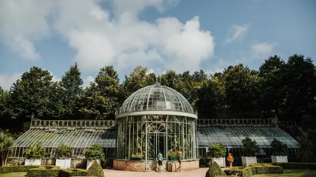 Geodesic greenhouse made of glass and metal surrounded by trees and gardens