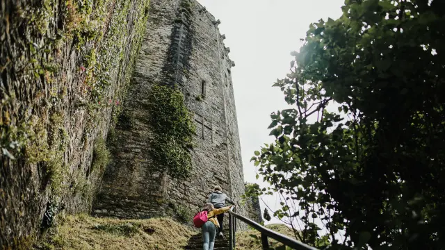 Person in hiking gear standing in front of a large rocky cliff in the mountains
