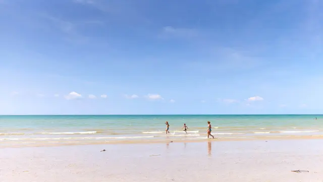 Three people walking on an empty beach at sunset
