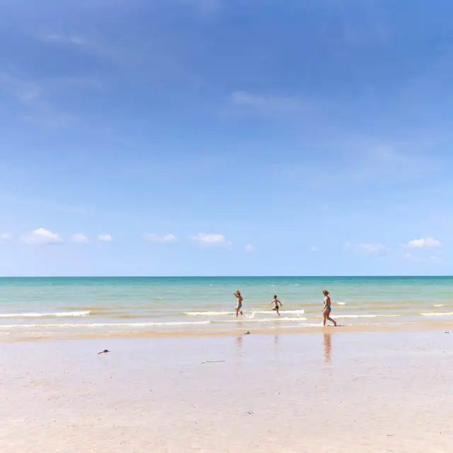 Drei Kinder laufen auf einem feinen Sandstrand