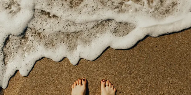 Deux pieds nus sur le sable avec des vagues qui s’échouent