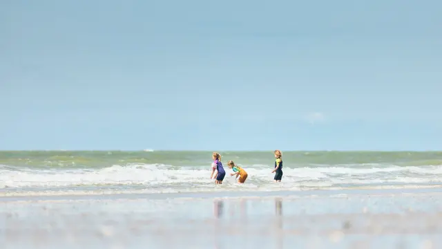 Trois enfants jouent dans les vagues sur une plage à Hauteville sur Mer