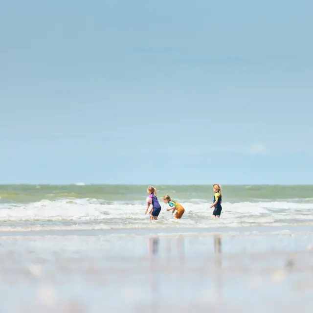 Drei Kinder spielen in den Wellen am Strand