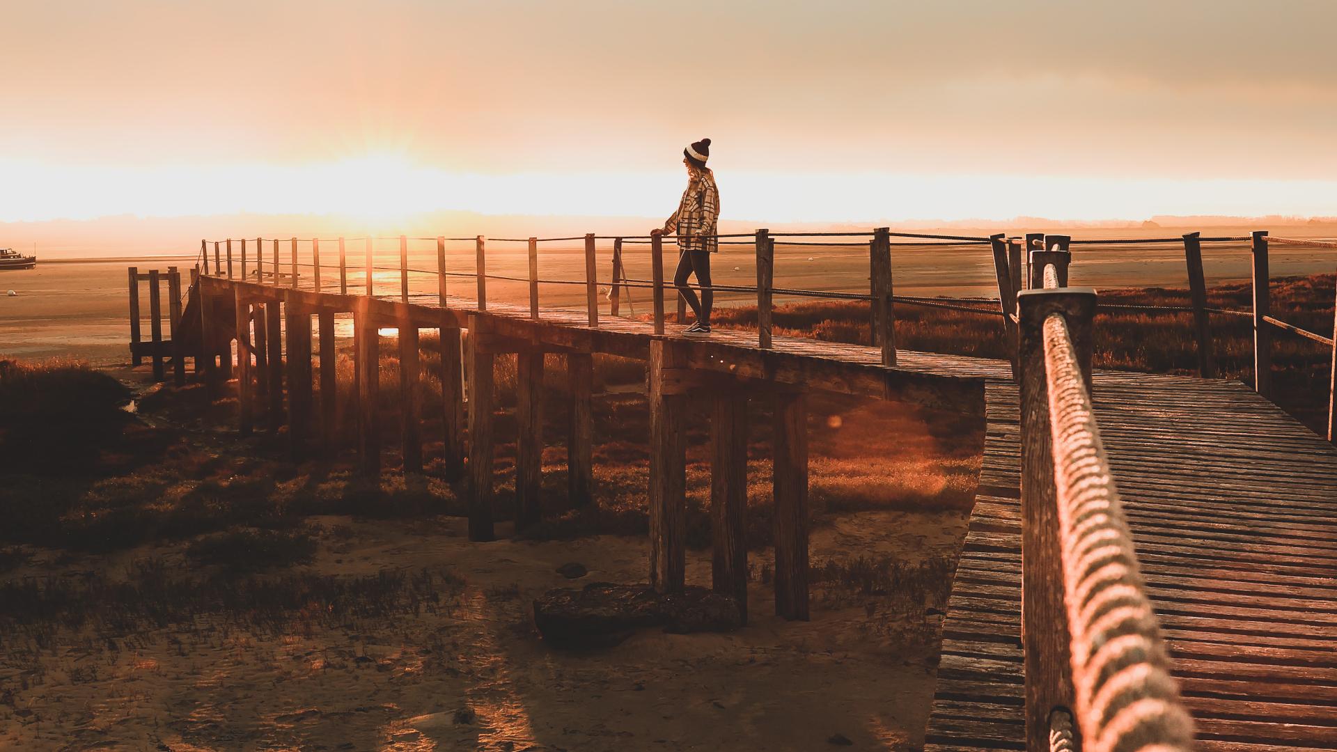 Une personne debout sur une passerelle en bois au coucher du soleil