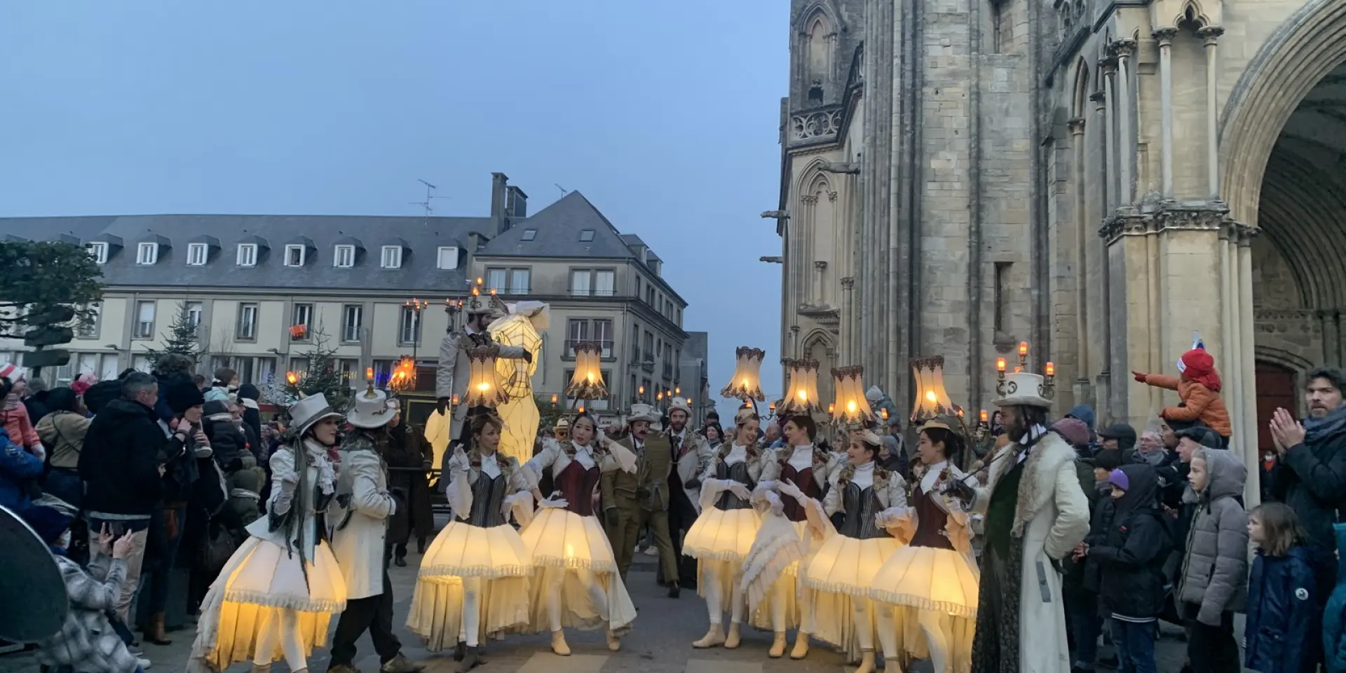 Groupe de personnes en costumes traditionnels avec des lanternes devant une cathédrale