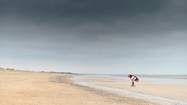 Personne pratiquant le kitesurf sur une plage avec un cerf-volant rouge