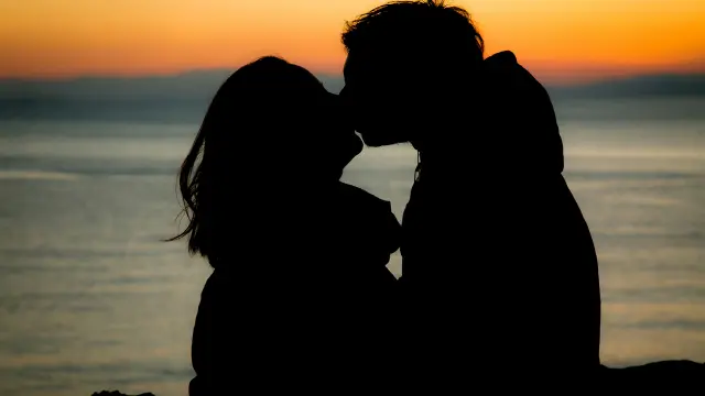 Deux silhouettes de personnes assises sur un quai face à un coucher de soleil sur la mer