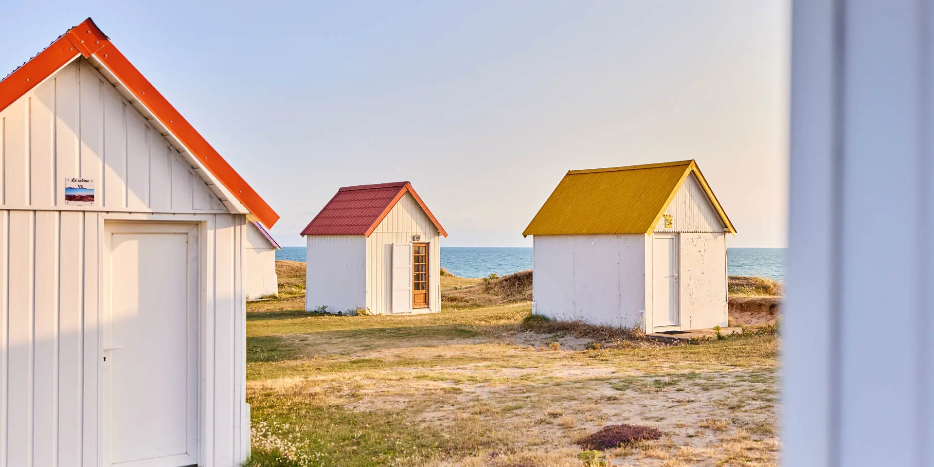 Trois cabines de plage avec des toits de couleurs différentes à Gouville sur Mer