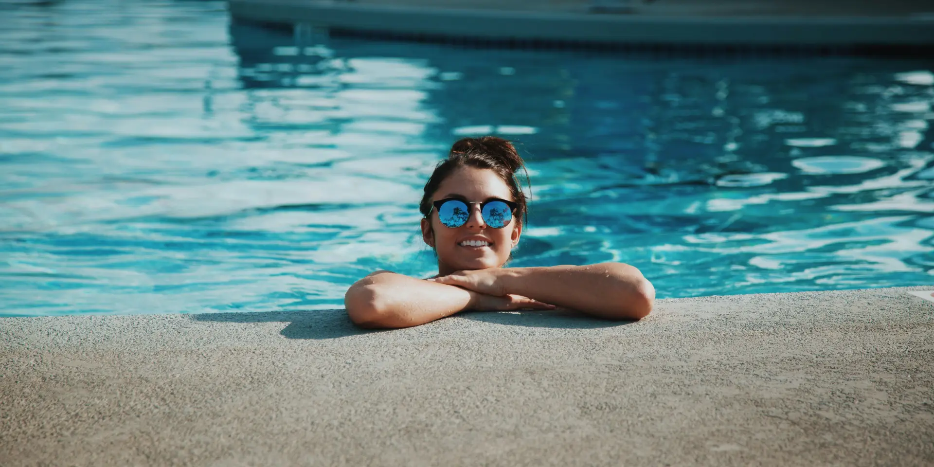 Femme souriante avec des lunettes de soleil, allongée au bord d'une piscine
