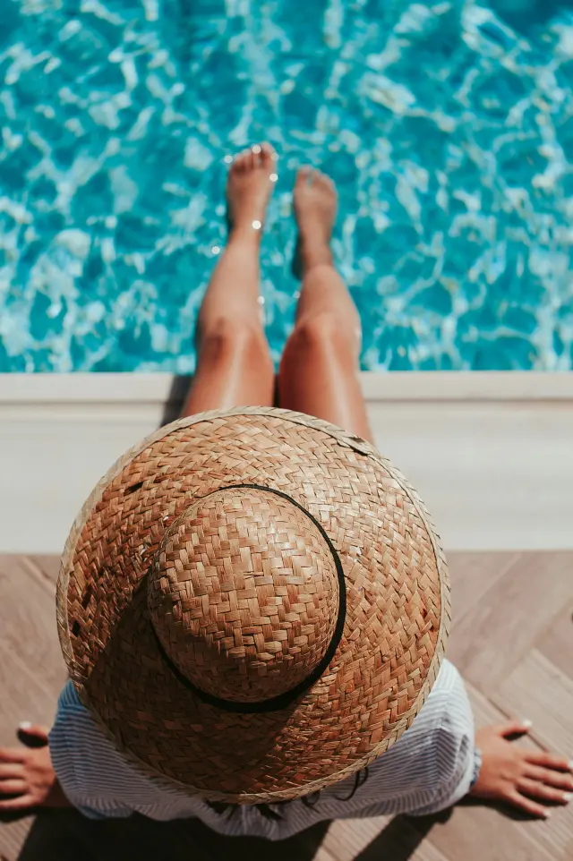 Personne en short et chapeau de paille allongée au bord d'une piscine