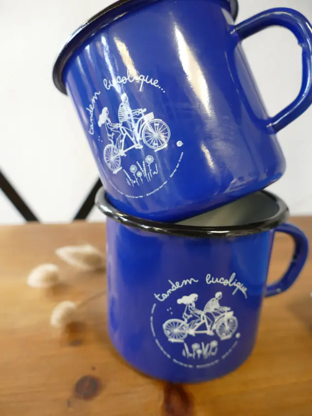 Deux tasses en métal bleu avec des illustrations de vélos et des inscriptions en français : mug émaillés