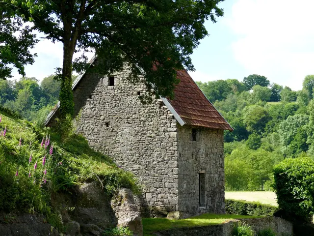 Maison en pierre avec toit rouge entourée d'arbres et de végétation