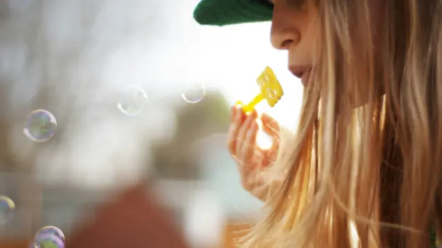 Enfant avec un chapeau vert soufflant des bulles de savon
