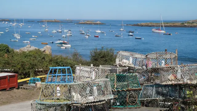 Filets de pêche empilés près d'un port avec des bateaux en arrière-plan à Chausey