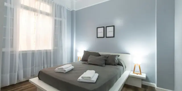 Chambre d'hôtes avec lit double, rideaux blancs et murs gris